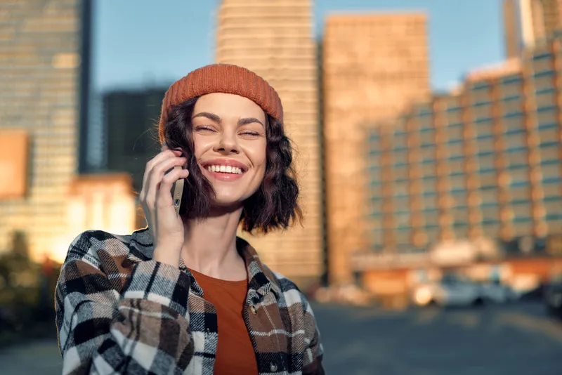 Woman smile phone urban city portrait sunlight happiness captured in candid lifestyle with authenticity, emotional storytelling and warm golden hour glow, mindful living mood.