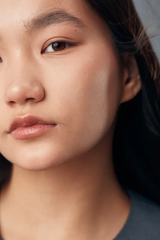 Portrait of serious young woman with natural skin looking at camera closeup. Female face with smooth complexion, dark eyes and relaxed expression on neutral background.