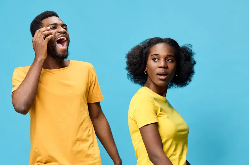 Excited diverse couple with bright yellow outfits expressing joy against a vibrant blue background, showcasing happiness and connection in a modern style