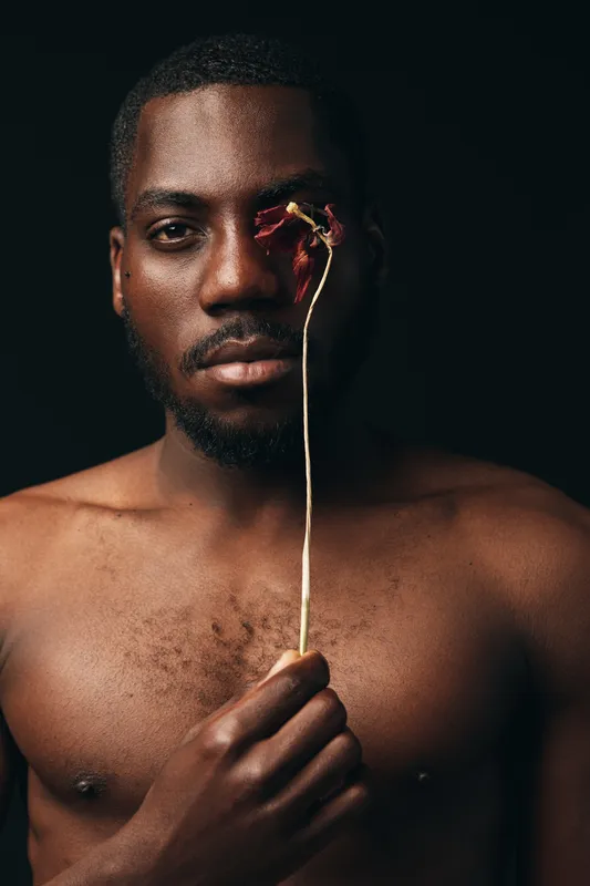 Creative conceptual portrait of African man holding dried flower near face with dark background, artistic visual style, closeup, emotion and expression in studio lighting.