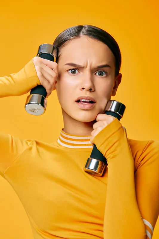Fitness woman workout with dumbbells in a vibrant yellow studio, displaying strength, focus and energetic training as she powers through a precise exercise routine.