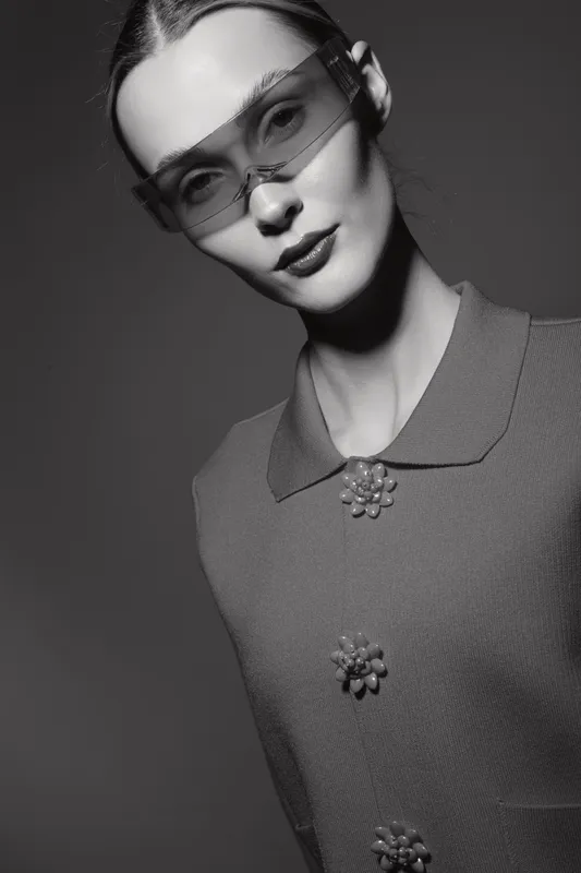 Young caucasian woman with pale skin wearing vintage dress and modern sunglasses looks at camera in black and white fashion portrait.