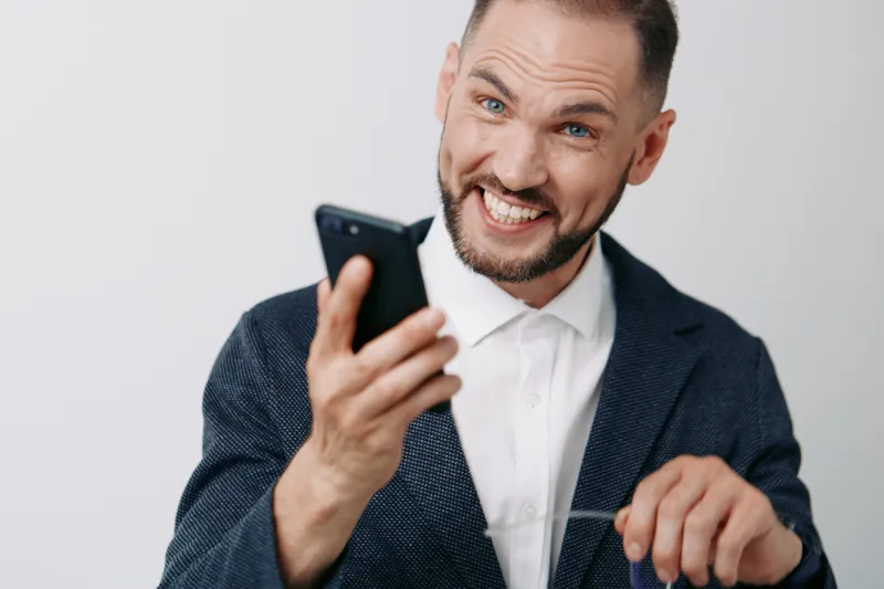 A professional businessman in a dark blazer and white shirt smiles broadly, holding a smartphone. Isolated colorful background enhances a confident, energetic mood and a modern, approachable