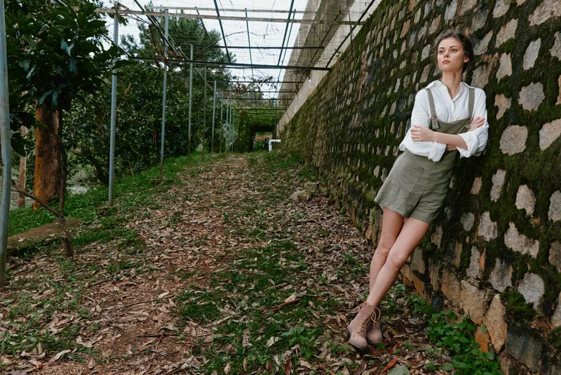 Stylish young woman in a garden showcasing summer fashion with a relaxed pose and natural surroundings, highlighting seasonal style and earthy tones