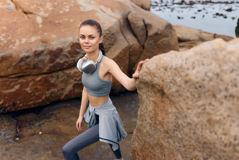 Young athletic woman in activewear climbing rocky terrain near the sea, showcasing determination and strength in a natural setting