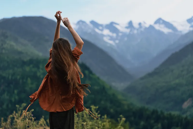 Person standing with arms raised in a vast mountain landscape, enjoying nature and an open sky. The scene conveys freedom, adventure and a peaceful outdoor moment.