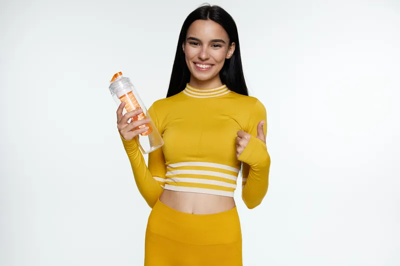 smiling woman sport fitness wearing yellow athletic outfit holding water bottle showing thumbs up, healthy lifestyle, hydration, energy boost, positive attitude