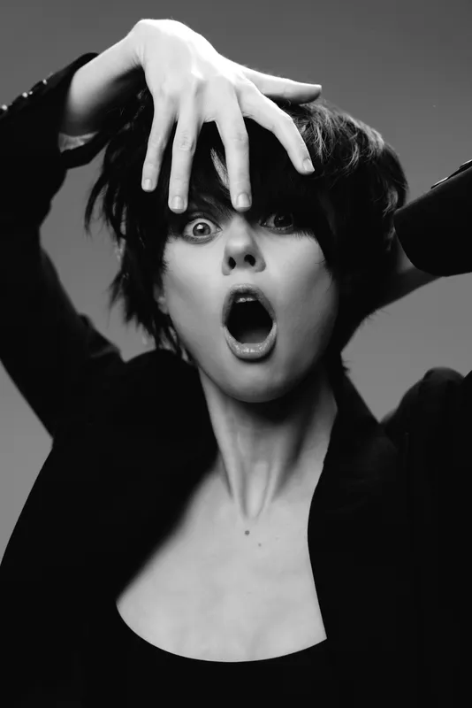 Black and white portrait of shocked woman with short dark hair expressing surprise and emotion in studio setting.