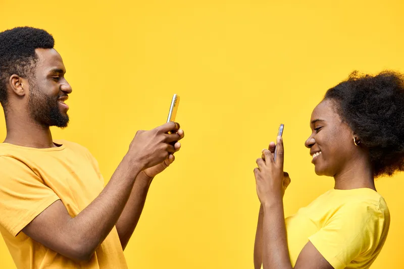 Two young friends taking selfies on their smartphones, wearing matching yellow outfits, against a vibrant yellow background, showcasing joy and modern communication