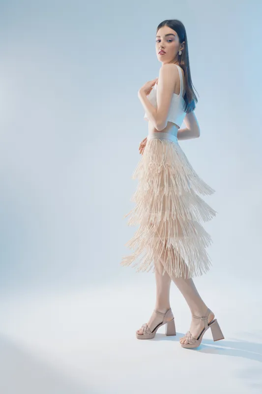Young woman beauty fashion posing in a white top and fringed skirt. Studio shot with soft lighting on a light background. Concept for style, elegance, and modern trends.