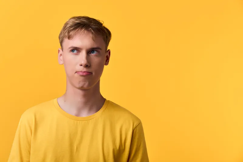 Thinking man in a yellow shirt against a bright yellow backdrop, puzzled expression, contemplating ideas, focused mood and curiosity in a minimal studio setting