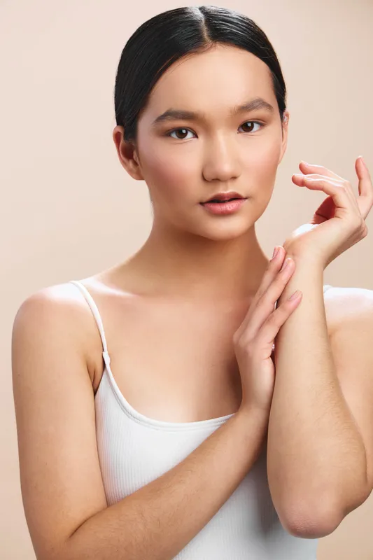 asian woman wearing a white top is captured in a close up portrait with soft lighting, smooth skin, and a calm expression against a clean minimalist background.