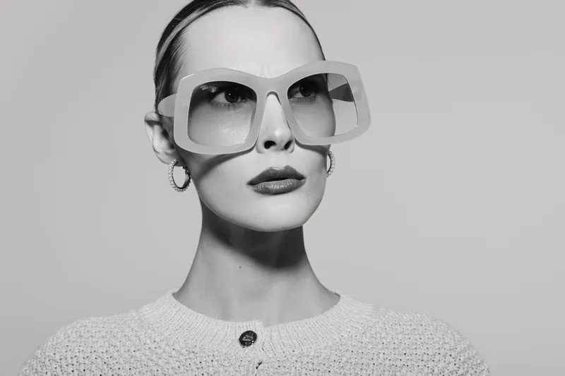 Stylish white woman with pale skin and slicked back hair wearing oversized sunglasses and knitted top. Fashion portrait in black and white studio concept for modern style.