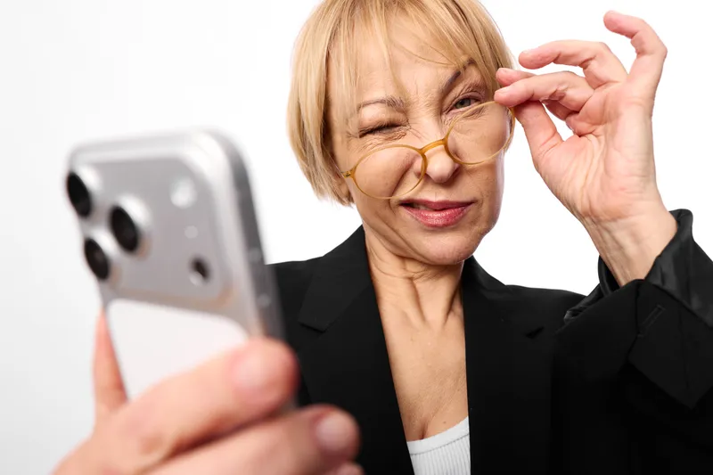 Woman, senior, glasses, smartphone, hand, smiling, communication, technology, indoors, portrait, soft light, she adjusts glasses while holding phone, calm modern life