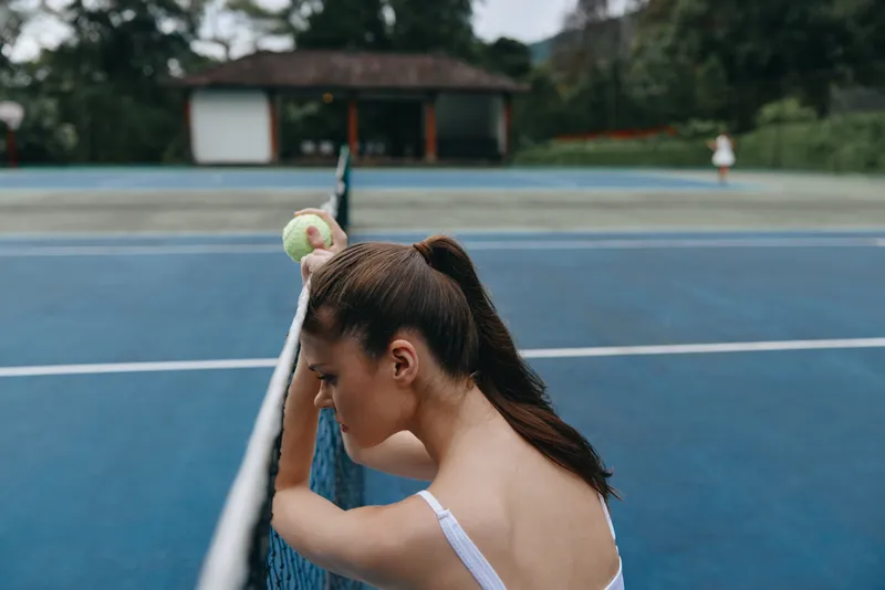 Portrait of a focused young female tennis player holding a ball, showing determination on a blue outdoor tennis court