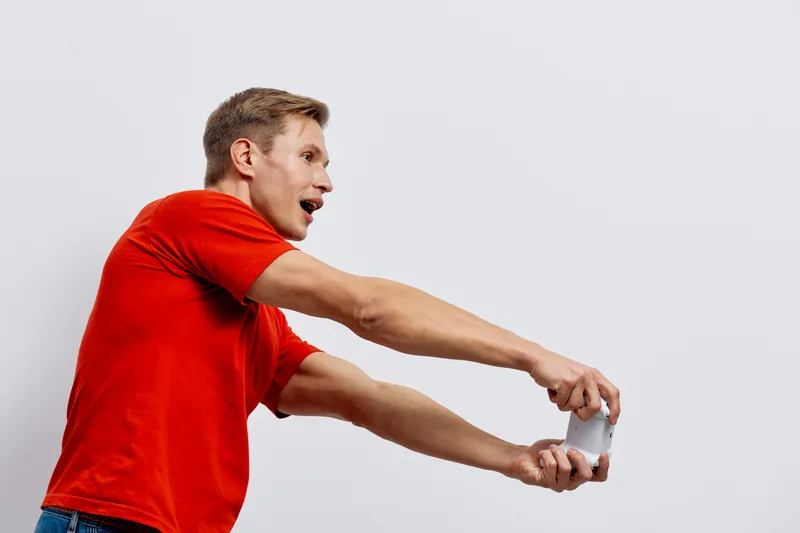 Casual man taking a selfie with mobile phone, expressing excitement and enthusiasm, wearing a bright red t-shirt, isolated on plain white background, studio portrait, lifestyle concept.