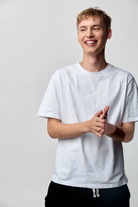 Cheerful young man in a white tee smiling and clapping, casual style, positive mood, studio shot capturing friendly reception and relaxed interaction with bright lighting