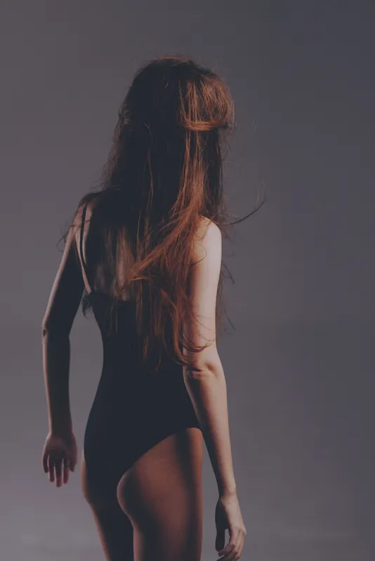 Woman with long hair in black bodysuit standing against dark gray background