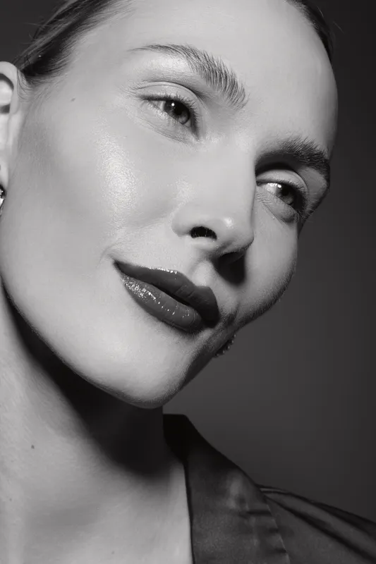 Close-up portrait of a fair-skinned Caucasian woman with glossy lips and clear skin looking away. Studio lighting highlights natural beauty and facial features in black and white.