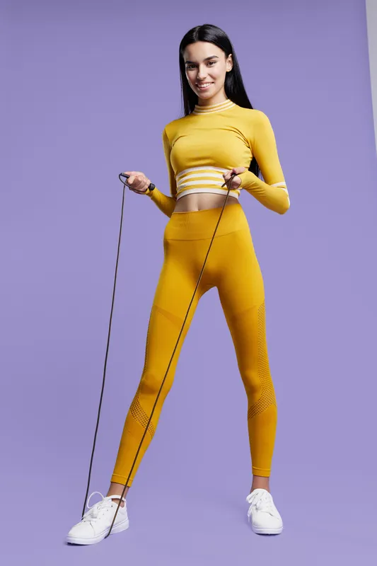 Sport fitness woman in yellow activewear practices jump rope exercise, showing energy, health, and wellness on a purple background with a focused and happy expression.