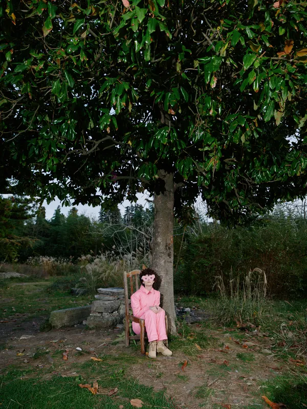 Girl sitting beneath a large tree on a bench in a park, wearing a pink dress, enjoying a quiet moment in a calm rural outdoor landscape with gentle daylight and nature
