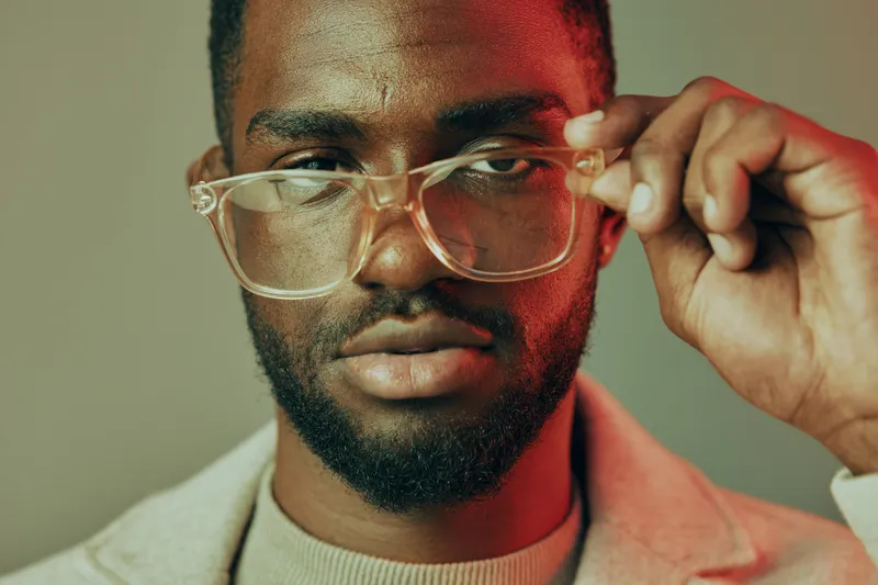 A confident young man adjusting his stylish eyeglasses, showcasing modern fashion, expressive emotions, and a vibrant color palette for contemporary lifestyle photography