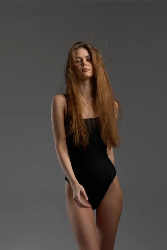 tall woman in black leotard with long hair posing against gray background