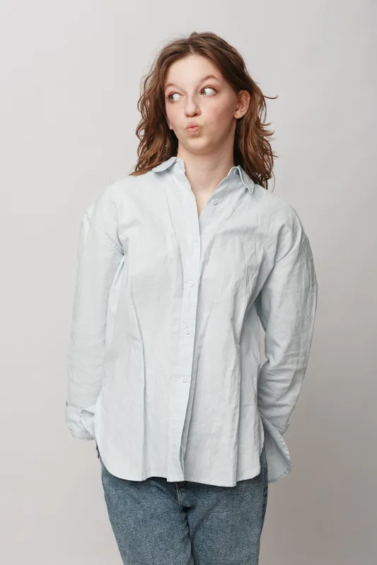 Young woman in white shirt and blue jeans looks sideways with a playful expression. Casual outfit and natural makeup on neutral background. Concept of youth, fashion, and personality.