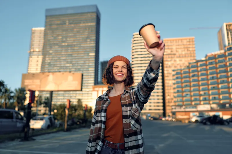 Woman coffee city smile beanie urban candid golden moment: woman with coffee in city street, smile and beanie in urban scene, candid lifestyle and authenticity with golden hour glow and emotional