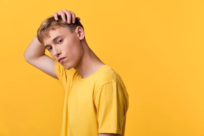 Yellow shirt, yellow background, confused expression, pensive mood, head scratching, casual fashion, studio photography, youth style in a controlled studio setup, capturing a modern minimalist mood