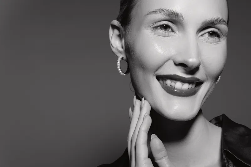 Close-up portrait of a happy white woman with light skin smiling and touching her face in black and white studio. Concept of beauty, skincare, and joyful expression.