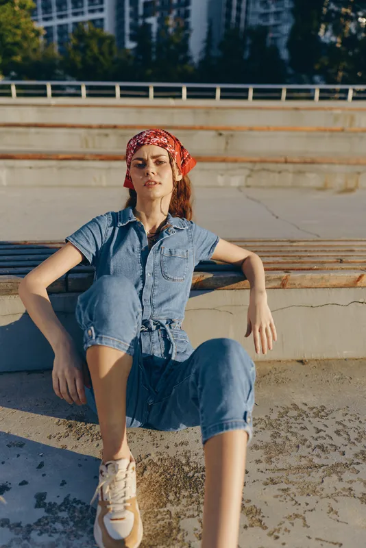 lifestyle woman in modern boho-western denim street style sitting relaxed outdoors, film color tones, casual outfit with red bandana and sneakers, sunny day mood