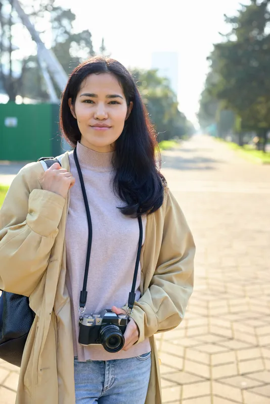 Camera, woman, outdoor, daylight, casual jacket, street path, travel photography, lens, candid moment capturing exploration and creativity in bright surroundings, backpack, soft sunlight, relaxed