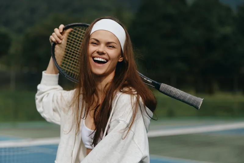 Happy young woman in sportswear laughing on a tennis court, showcasing athletic style and joy in outdoor sports activities