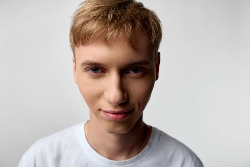Young man with blond hair wearing a white tee, close up face, soft studio lighting, neutral background, calm expression, natural and clean look for fashion or lifestyle projects
