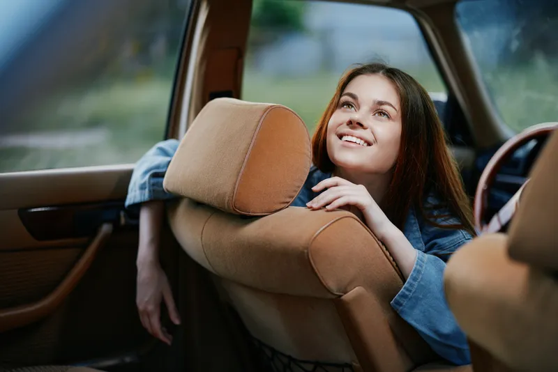 Young woman smiling in a comfortable car interior, featuring natural light and warm tones, portraying joy and relaxation during a road trip.