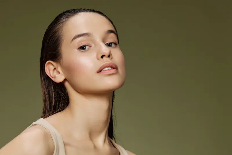 Elegant young model with natural makeup and long hair against a soft green background, showcasing beauty and confidence in a minimalist style