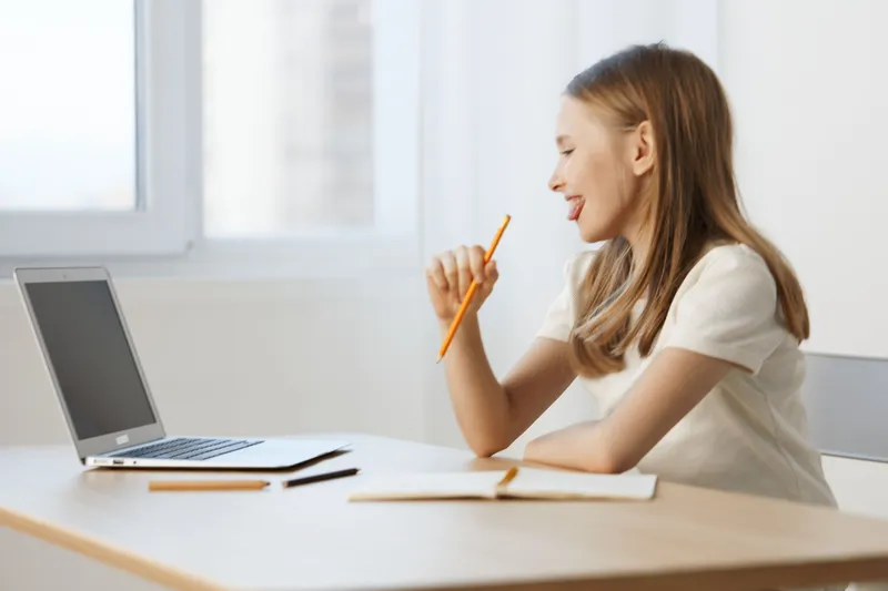 Young woman working on a laptop, smiling with a pencil in hand, bright and airy workspace, capturing creativity, inspiration, and productivity