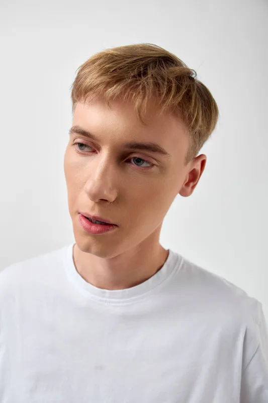 Man, thoughtful gaze in a white tee posing in a clean studio, soft lighting, subtle shadows, calm mood, casual fashion, simple background, focused expression, professional stock photography vibe