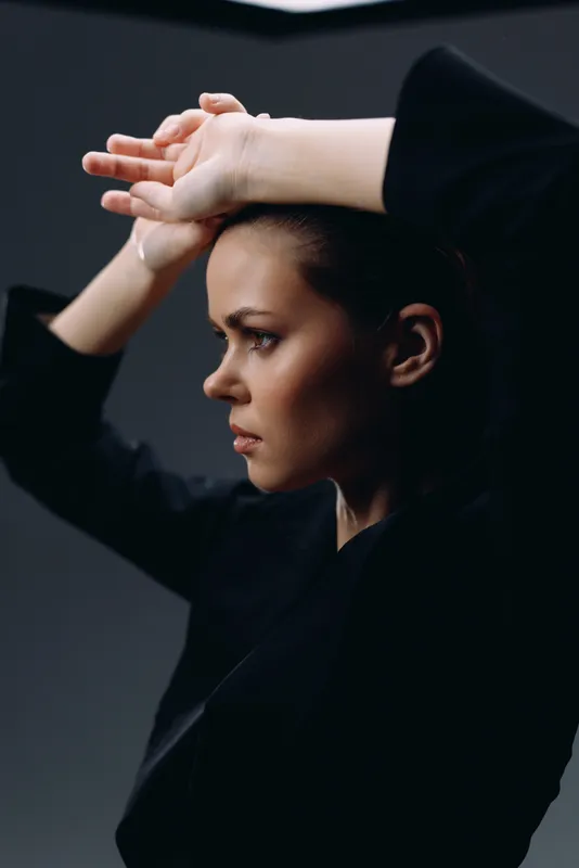 Serious woman with raised arms in black clothing against dark background expressing determination and focus.