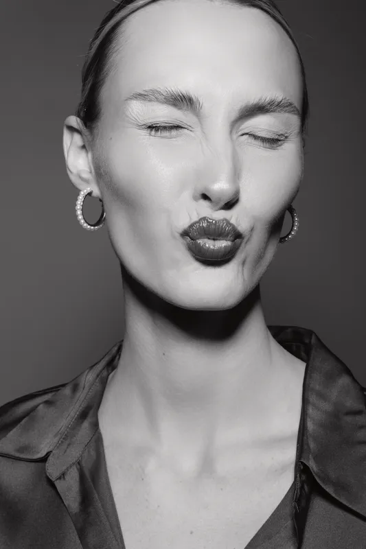Close-up of a white woman with fair skin puckering lips and closed eyes. Black and white portrait with earrings and casual shirt in studio.