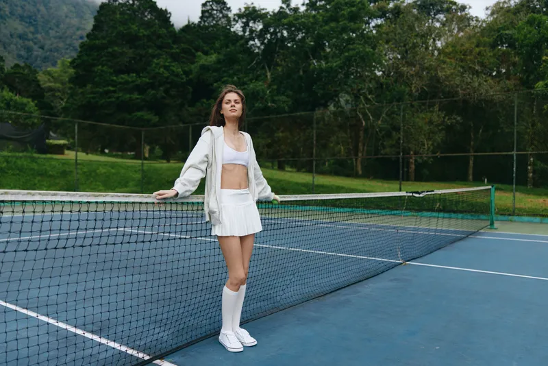 Young athlete woman in sporty outfit celebrating on a tennis court surrounded by greenery, exuding joy and vitality, perfect for sports and fitness themes