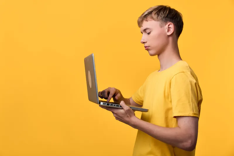 Man with a laptop in a bright yellow studio, demonstrating modern technology use for work and learning, online tasks and focus with a portable computer