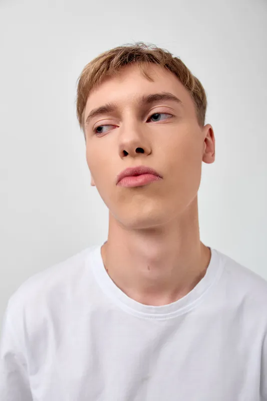 Young man in a white t shirt with a thoughtful expression, studio shot, clean lighting, minimal background, calm mood, contemporary fashion vibe.