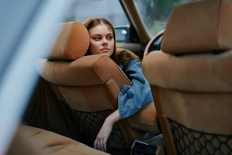 Pensive young woman in casual blue outfit relaxing in a luxurious car interior, reflecting on her thoughts with a serene expression.