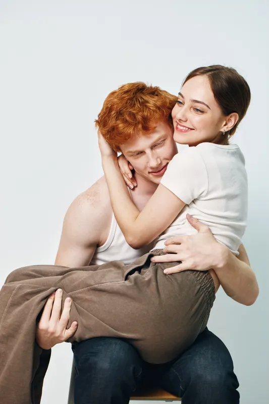 Couple in casual clothes with woman sitting on man's lap smiling and embracing in affectionate hug with love and happiness on white background studio.