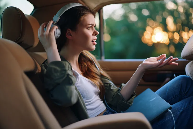 Young woman listening to music in a car, expressing emotions, wearing casual clothing, with a soft green background highlighting creativity and relaxation.