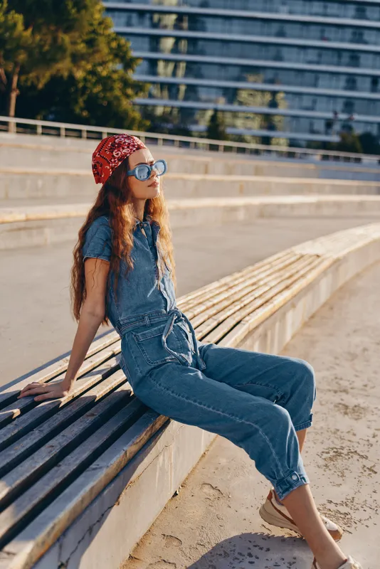 lifestyle woman in modern boho-western denim street style sitting outdoors wearing sunglasses and red bandana with film color warm tones under sunlight