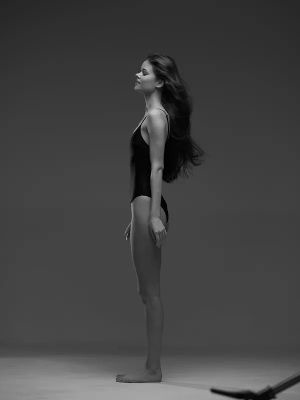 Black and white profile of a tall slender woman standing with closed eyes against a neutral background