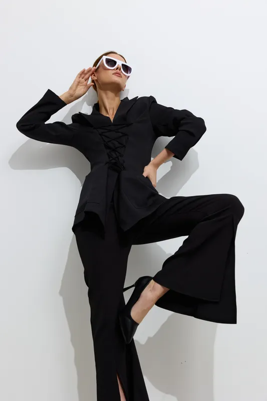Fashion woman in black outfit posing confidently against white background, wearing stylish sunglasses and displaying modern elegance and attitude.